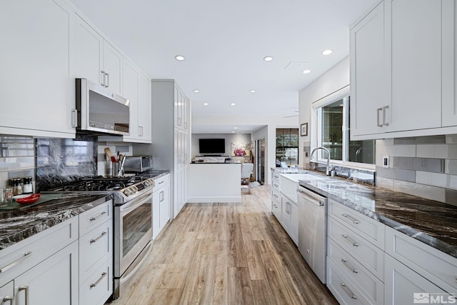 kitchen featuring stainless steel appliances, a sink, light wood-type flooring, decorative backsplash, and dark stone countertops