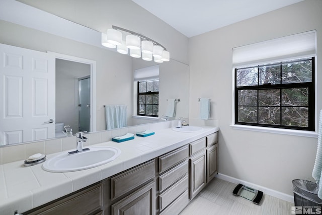 full bathroom with double vanity, baseboards, toilet, and a sink