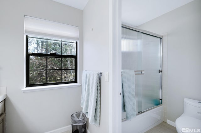 bathroom featuring toilet, shower / bath combination with glass door, baseboards, and vanity