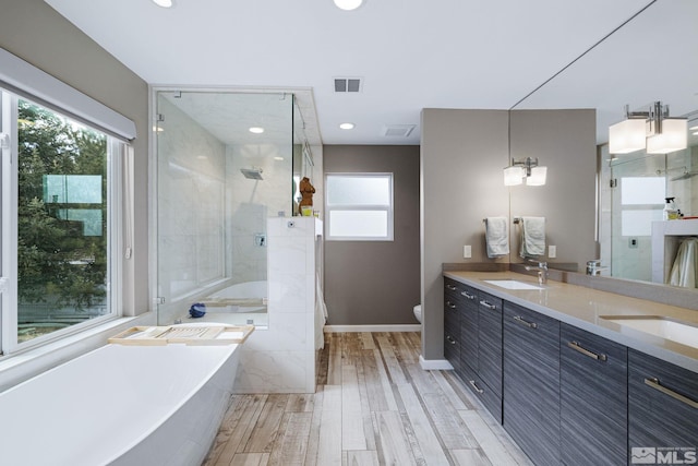 full bath featuring visible vents, a stall shower, a sink, wood finished floors, and a freestanding tub