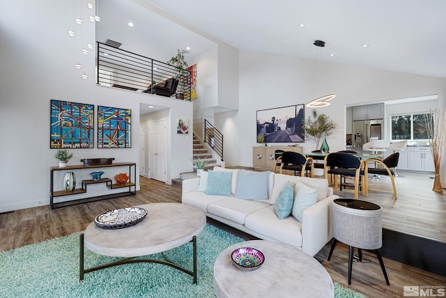 living room featuring visible vents, wood finished floors, high vaulted ceiling, baseboards, and stairs