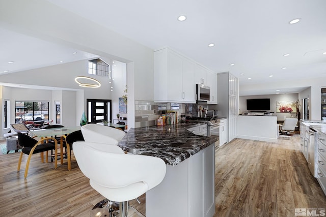 kitchen with stainless steel appliances, light wood-style flooring, open floor plan, white cabinets, and dark stone counters