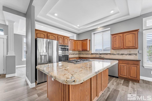 kitchen with decorative columns, tasteful backsplash, appliances with stainless steel finishes, a tray ceiling, and a sink