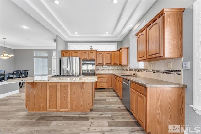 kitchen featuring a center island, a raised ceiling, appliances with stainless steel finishes, light wood-style floors, and a sink