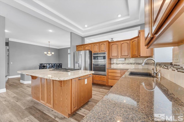 kitchen featuring stainless steel appliances, a sink, light stone countertops, a tray ceiling, and light wood finished floors