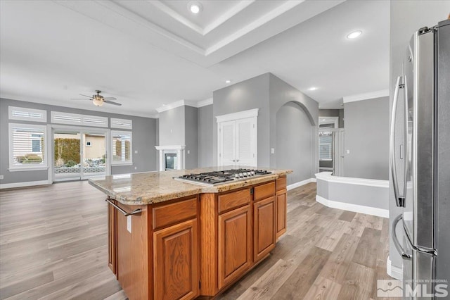 kitchen with stainless steel appliances, a kitchen island, light wood-style floors, open floor plan, and brown cabinetry