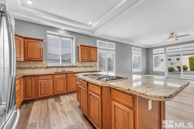 kitchen with light wood finished floors, appliances with stainless steel finishes, a center island, a sink, and backsplash