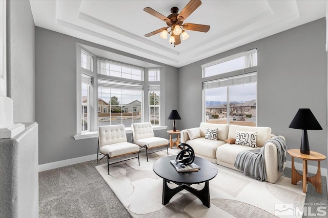 living room featuring a tray ceiling, carpet, a ceiling fan, and baseboards