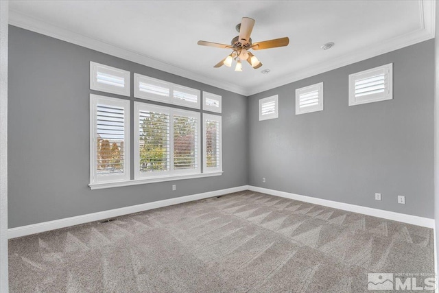 carpeted spare room with visible vents, crown molding, baseboards, and ceiling fan