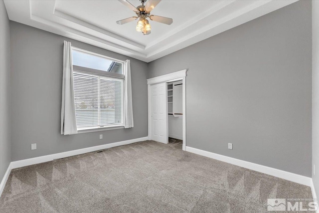 unfurnished bedroom with baseboards, a closet, a tray ceiling, and carpet flooring