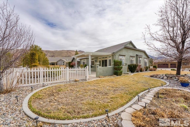 exterior space with a yard, a fenced front yard, a mountain view, and stucco siding