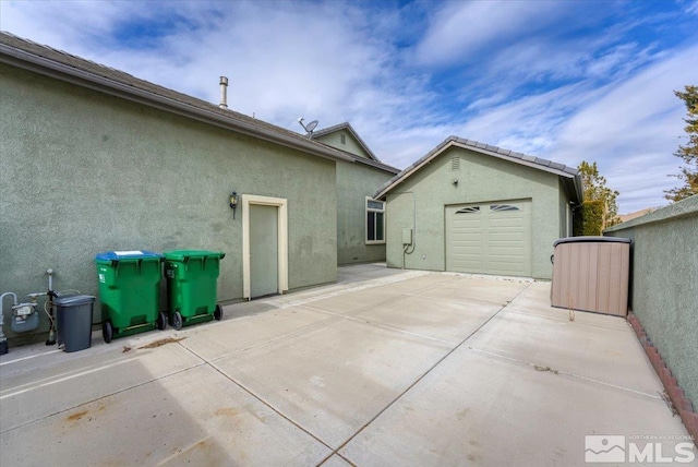 view of side of home with an outdoor structure, driveway, a detached garage, and stucco siding