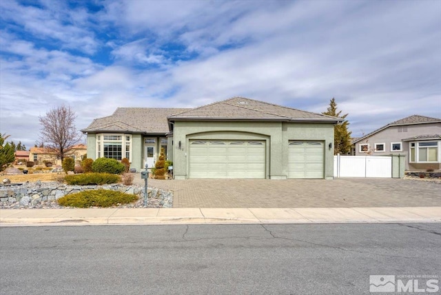 view of front of home with decorative driveway, fence, an attached garage, and stucco siding