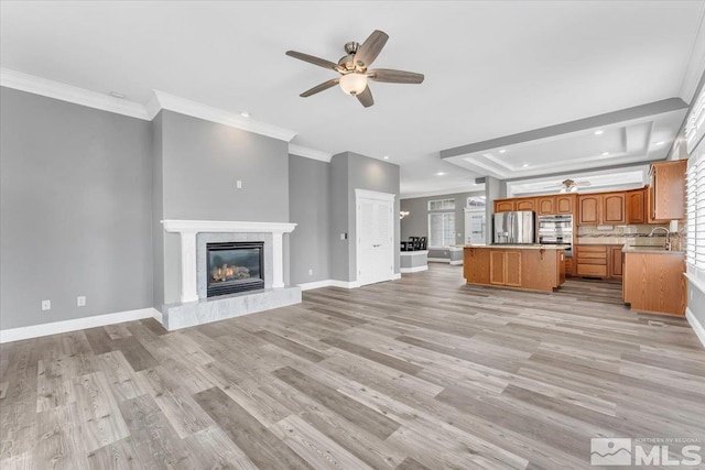 unfurnished living room featuring baseboards, a raised ceiling, a tile fireplace, crown molding, and a sink