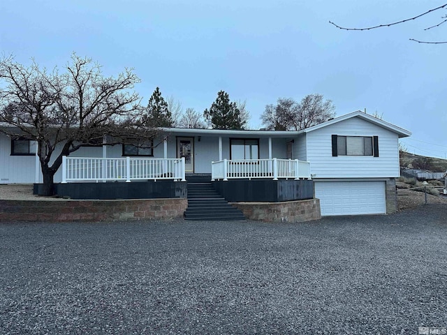 view of front facade with a porch, gravel driveway, an attached garage, and stairs