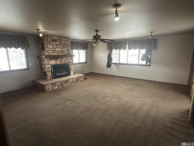 unfurnished living room featuring ceiling fan, a stone fireplace, carpet, and a healthy amount of sunlight