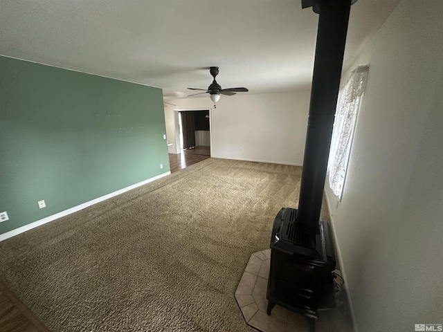 unfurnished living room featuring a wood stove, carpet, baseboards, and a ceiling fan