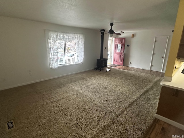 unfurnished living room with ceiling fan, a wealth of natural light, carpet, and a wood stove