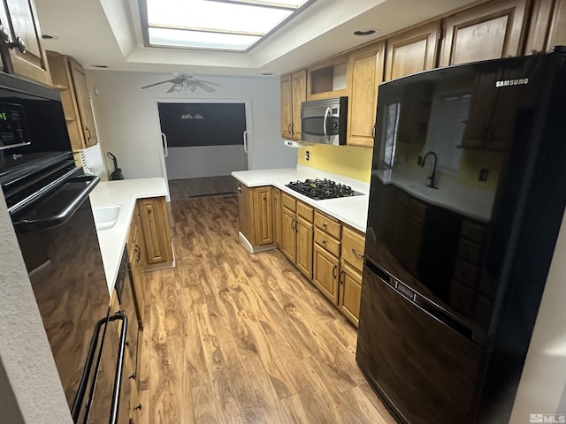 kitchen featuring light countertops, light wood-style floors, brown cabinetry, ceiling fan, and black appliances