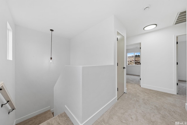 hall featuring carpet floors, an upstairs landing, visible vents, and baseboards