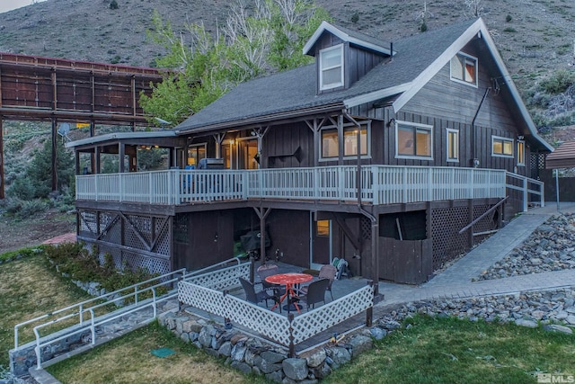 back of house with a shingled roof, a deck, and a patio