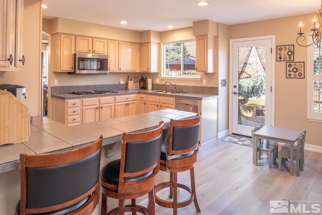 kitchen featuring appliances with stainless steel finishes, tile counters, light wood-type flooring, and a breakfast bar