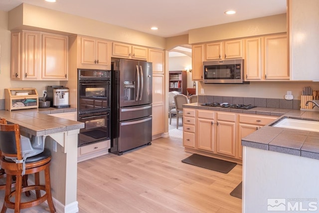 kitchen featuring arched walkways, appliances with stainless steel finishes, light wood-type flooring, and a sink