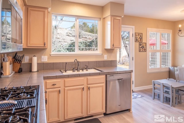 kitchen featuring stainless steel appliances, a sink, visible vents, tile counters, and light wood finished floors