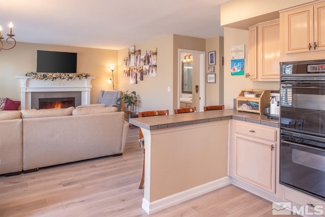 kitchen with dobule oven black, a tiled fireplace, open floor plan, light wood-type flooring, and a peninsula