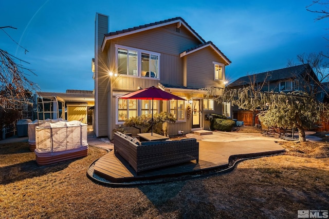 back of property at dusk featuring a deck, an outdoor living space, and a chimney