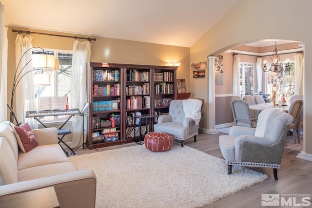 living room with arched walkways, a notable chandelier, lofted ceiling, wood finished floors, and baseboards