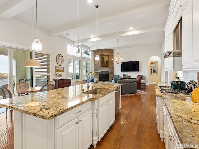 kitchen featuring arched walkways, a sink, a fireplace, stainless steel gas cooktop, and beam ceiling