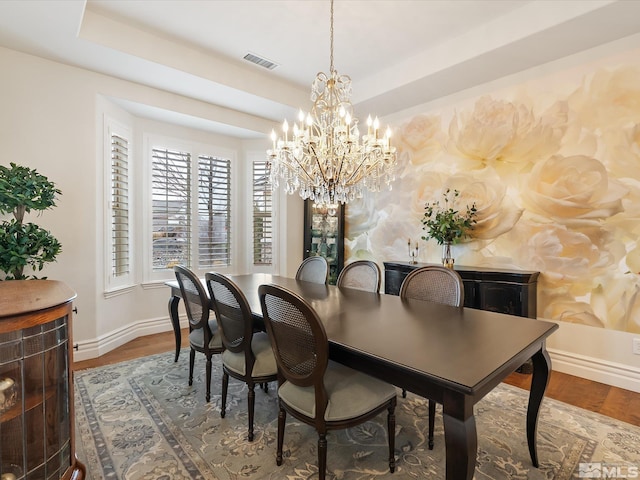 dining area featuring wood finished floors, visible vents, baseboards, a tray ceiling, and an inviting chandelier