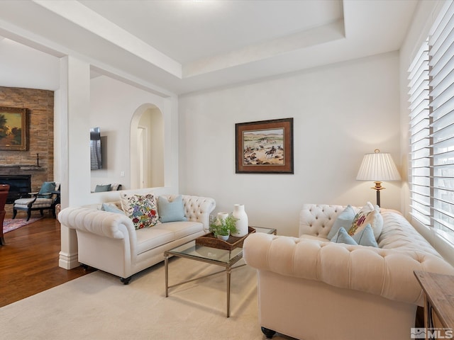 living room with arched walkways, a raised ceiling, a fireplace, and wood finished floors