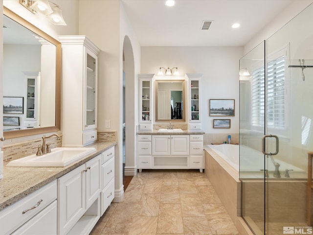 bathroom with a garden tub, visible vents, two vanities, and a sink