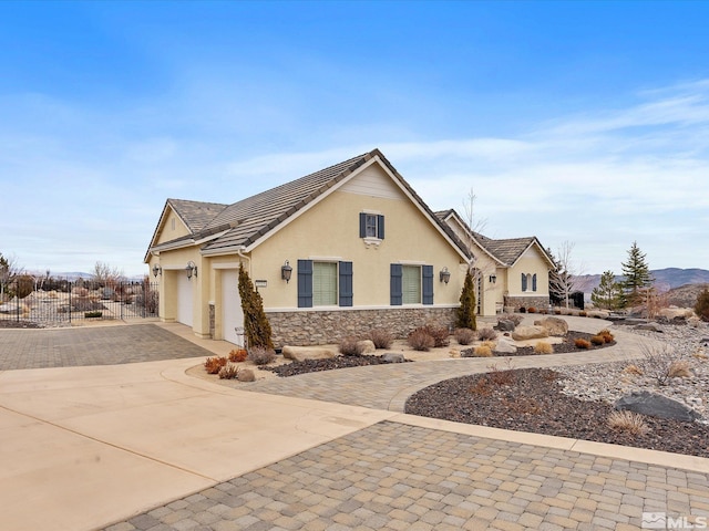 view of front facade with stucco siding, fence, a garage, stone siding, and driveway