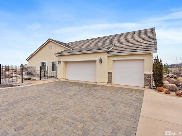 view of front of home with an attached garage, fence, stone siding, decorative driveway, and stucco siding