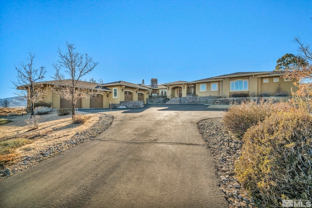 view of front of property featuring a garage, driveway, stone siding, and stucco siding