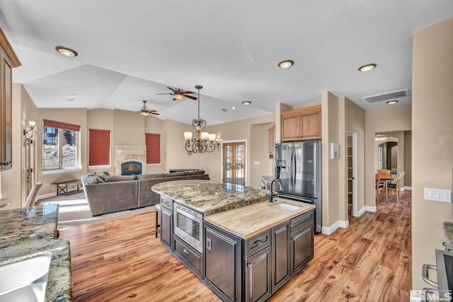 kitchen featuring a center island with sink, stainless steel appliances, lofted ceiling, visible vents, and a warm lit fireplace