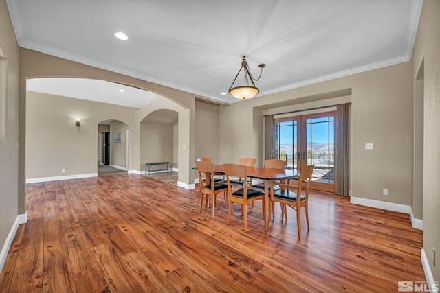 dining space featuring baseboards, arched walkways, wood finished floors, and ornamental molding