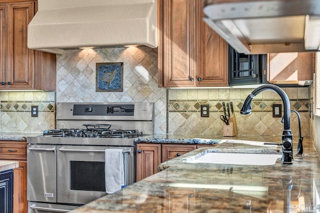 kitchen with light stone counters, extractor fan, a sink, double oven range, and brown cabinetry