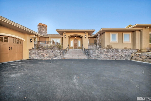 view of front facade with a garage, driveway, a chimney, and stucco siding