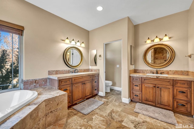 full bath with a bath, two vanities, a sink, and toilet