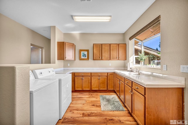 kitchen with a sink, visible vents, light wood-type flooring, brown cabinetry, and washer and clothes dryer