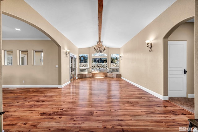 unfurnished dining area featuring vaulted ceiling with beams, a chandelier, arched walkways, wood finished floors, and baseboards