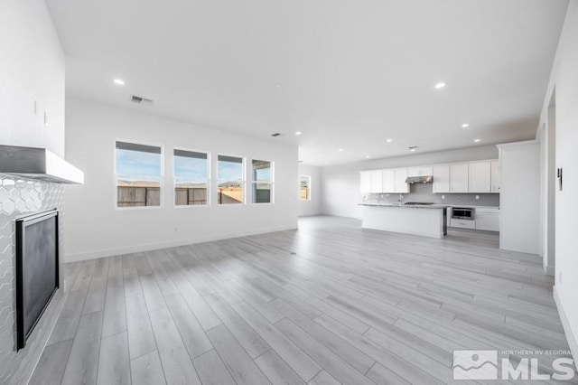 unfurnished living room with a fireplace, recessed lighting, visible vents, light wood-style flooring, and baseboards