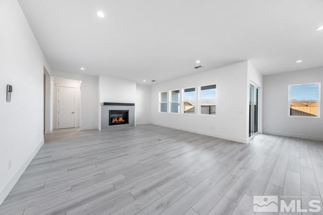 unfurnished living room featuring baseboards, light wood-type flooring, a glass covered fireplace, and recessed lighting