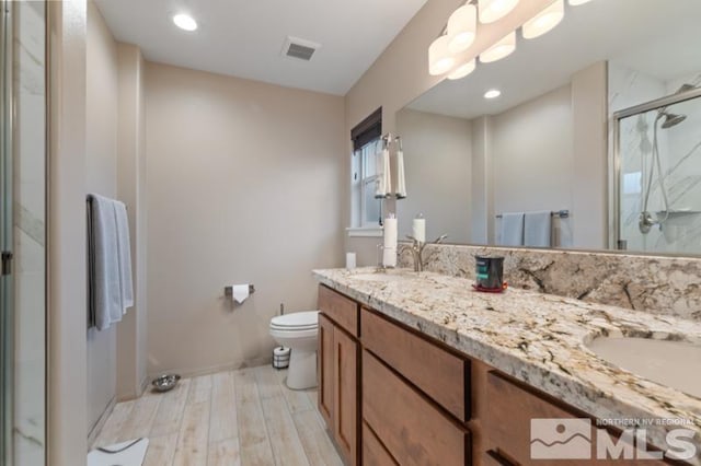 bathroom featuring wood finished floors, double vanity, a stall shower, a sink, and toilet