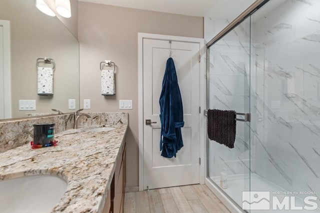 bathroom featuring double vanity, wood finished floors, a marble finish shower, and a sink