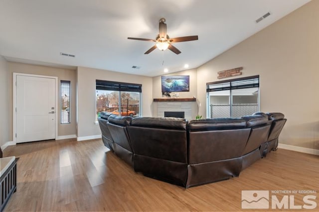 living area with baseboards, visible vents, a fireplace, vaulted ceiling, and light wood-type flooring